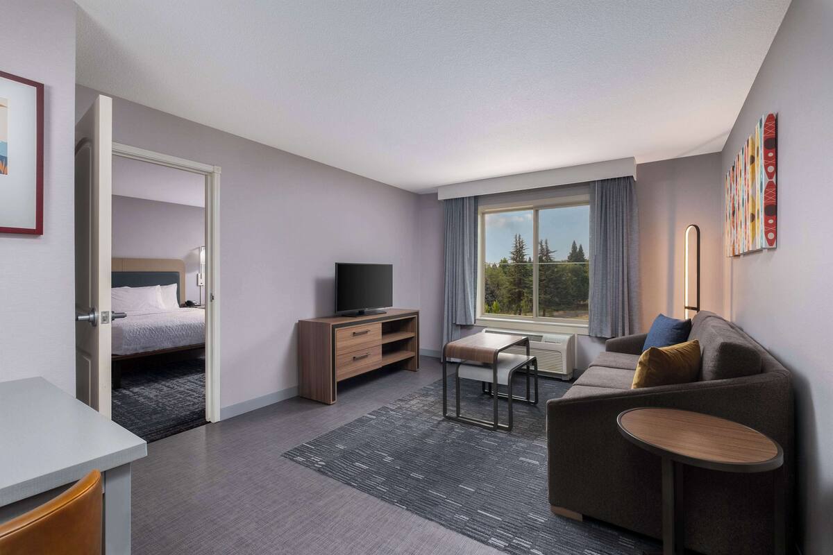 A modern hotel room with a bed, a desk, a sofa, and a TV.