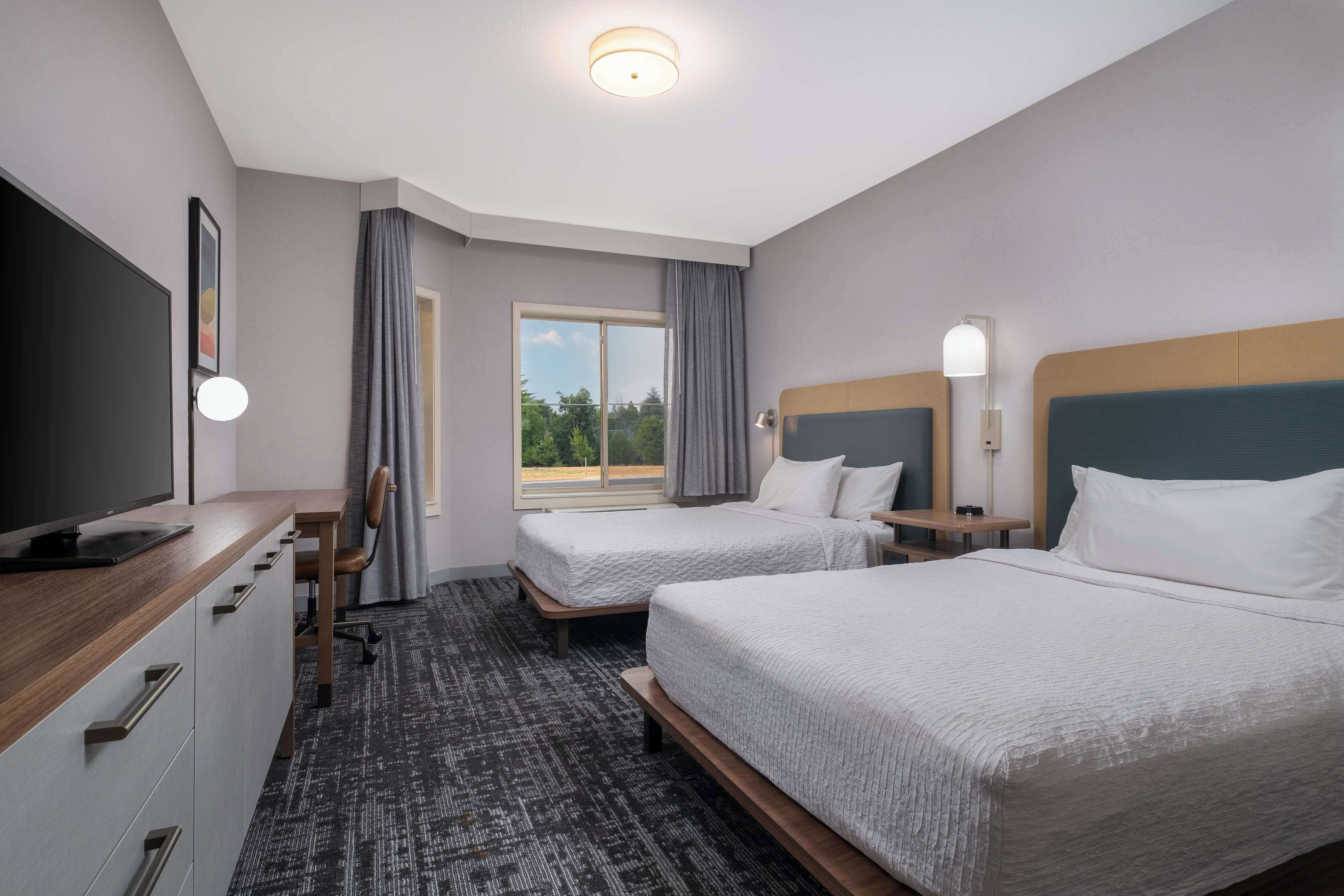 A hotel room with two beds, a desk, a chair, a TV, and a window with curtains.