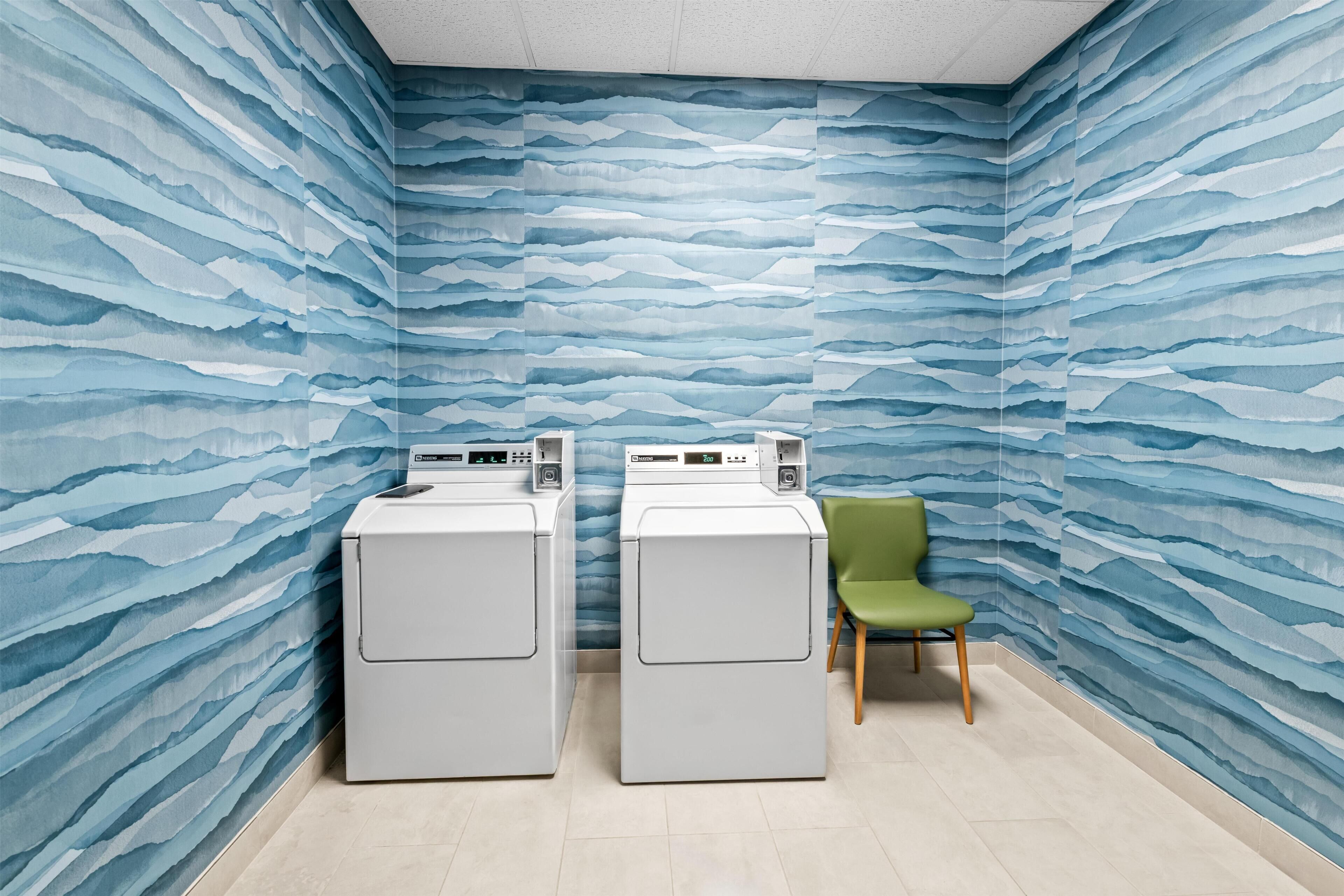 A laundry room with two washing machines and a chair.