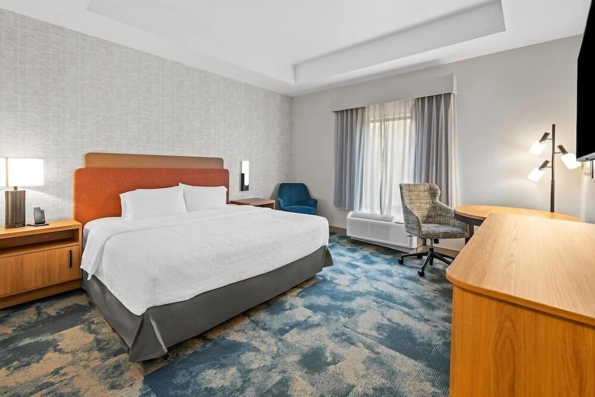 A hotel room with a bed, a desk, a chair, a TV, and a window with curtains.