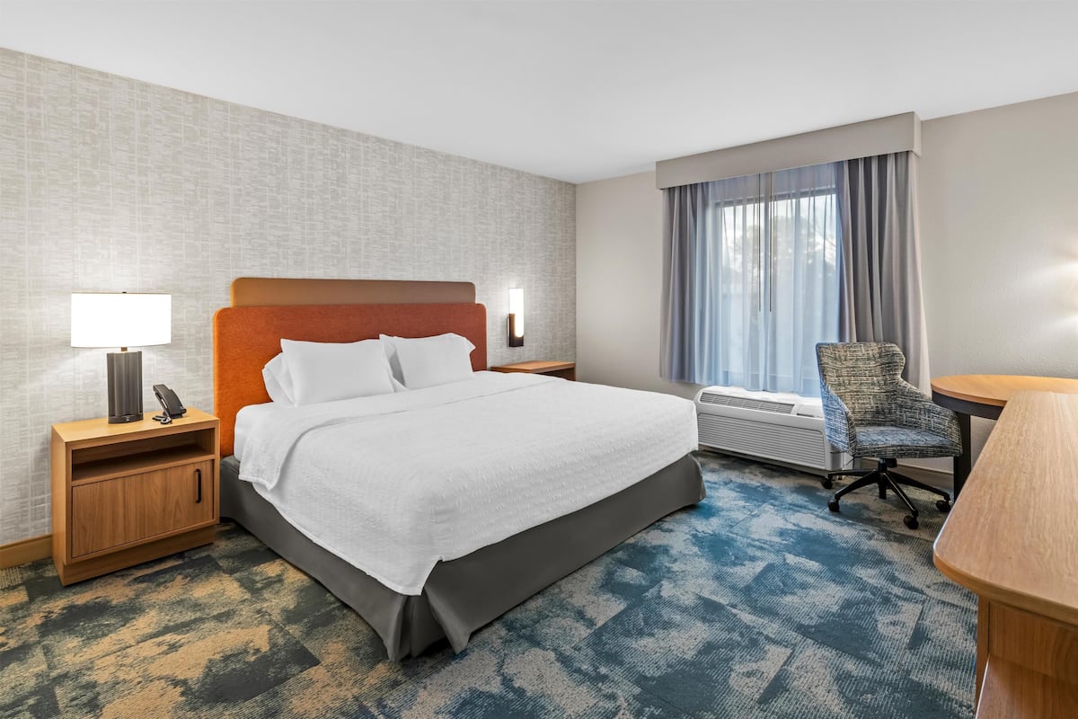 Habitación de hotel con cama, mesita de noche, lámpara, silla y ventana.