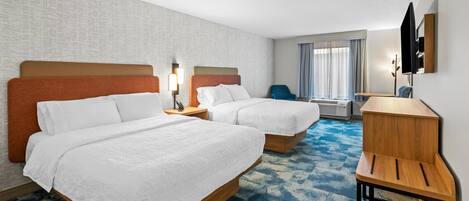 Quarto de hotel com duas camas, uma escrivaninha, uma cadeira, uma televisão e uma janela com cortinas.