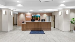 A hotel reception desk with a 'Welcome to Hampton' sign, a computer, a phone, and a blue mat on the floor. - Hampton Inn Harrison (Harrison)
