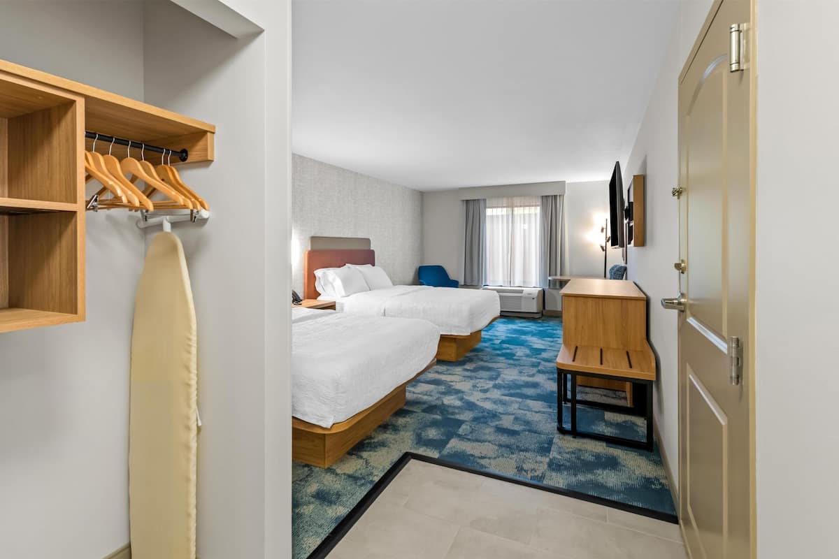 Habitación de hotel con dos camas, un escritorio, una silla, un televisor y un armario con perchas.