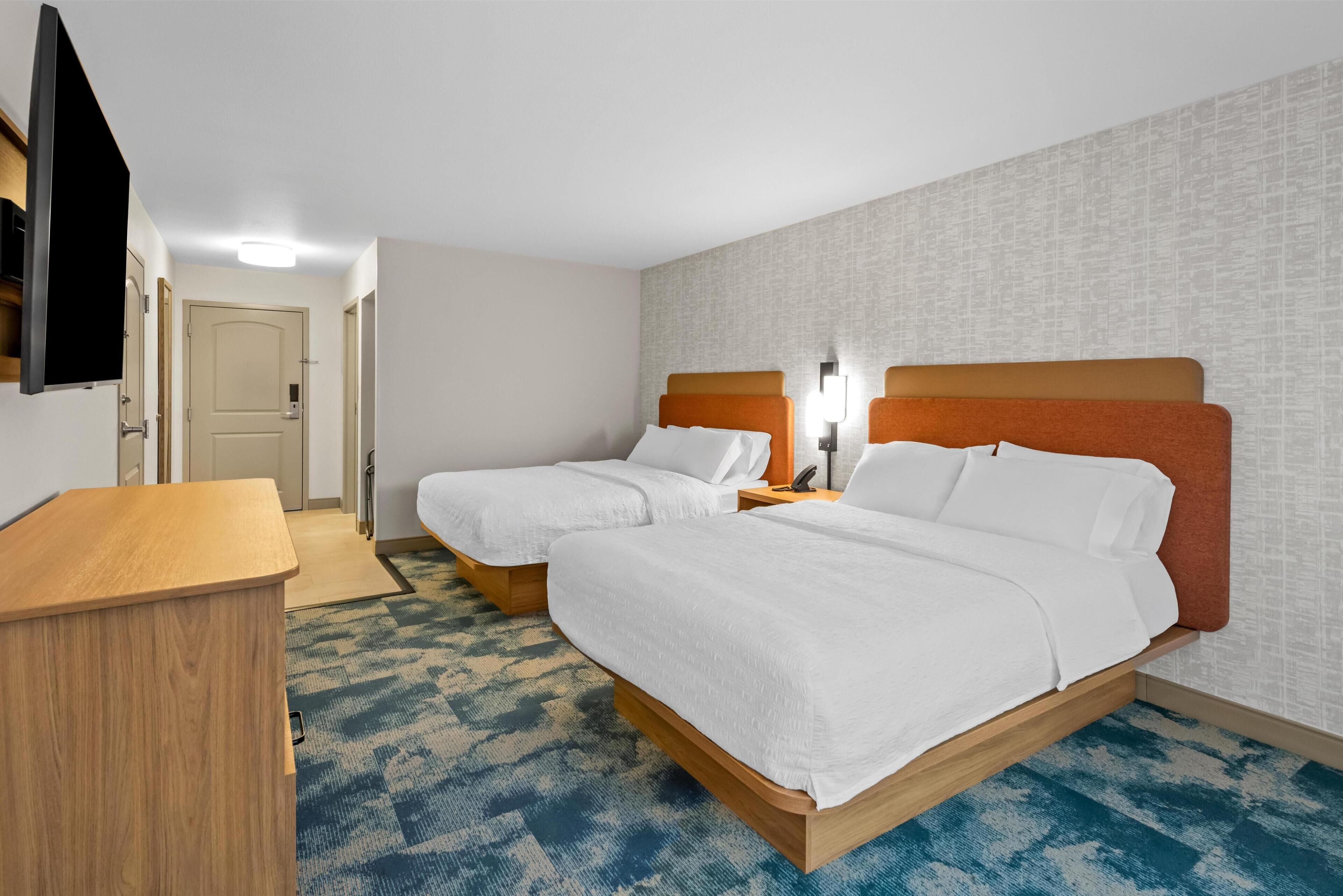 A hotel room with two beds, a desk, a TV, and a patterned carpet.