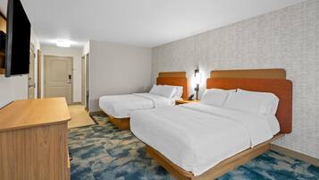A hotel room with two beds, a desk, a TV, and a patterned carpet.