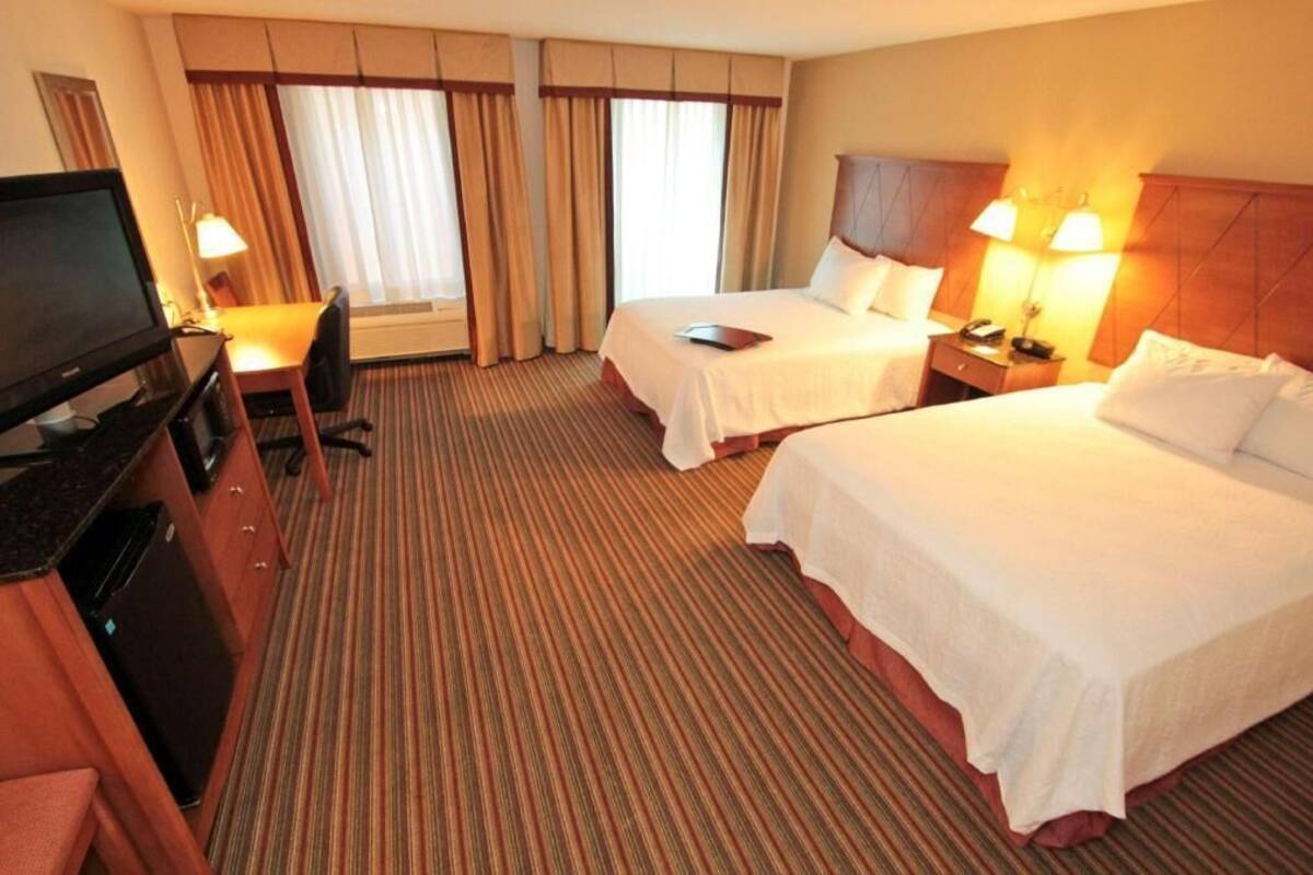 A hotel room with two beds, a desk, a television, and a window with curtains.
