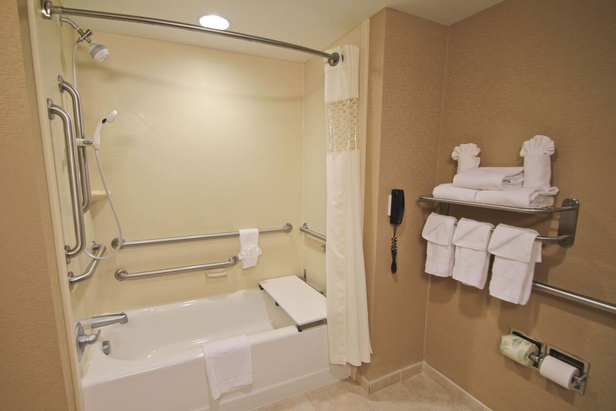 A bathroom with a walk-in shower, grab bars, a bathtub, and a towel rack with towels.