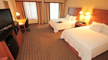 A hotel room with two beds, a desk with a computer, a TV, and a dining area with a chair and table.