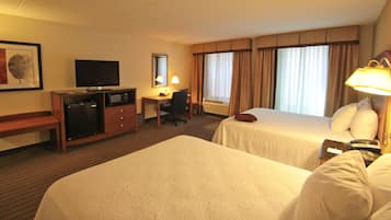 Een hotelkamer met twee bedden, een bureau met stoel, een televisie, een bureaulamp en een telefoon.