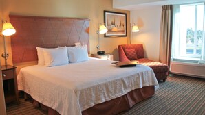 Habitación de hotel con una cama grande, dos lámparas de noche, una silla, una mesita y una ventana con cortinas.
