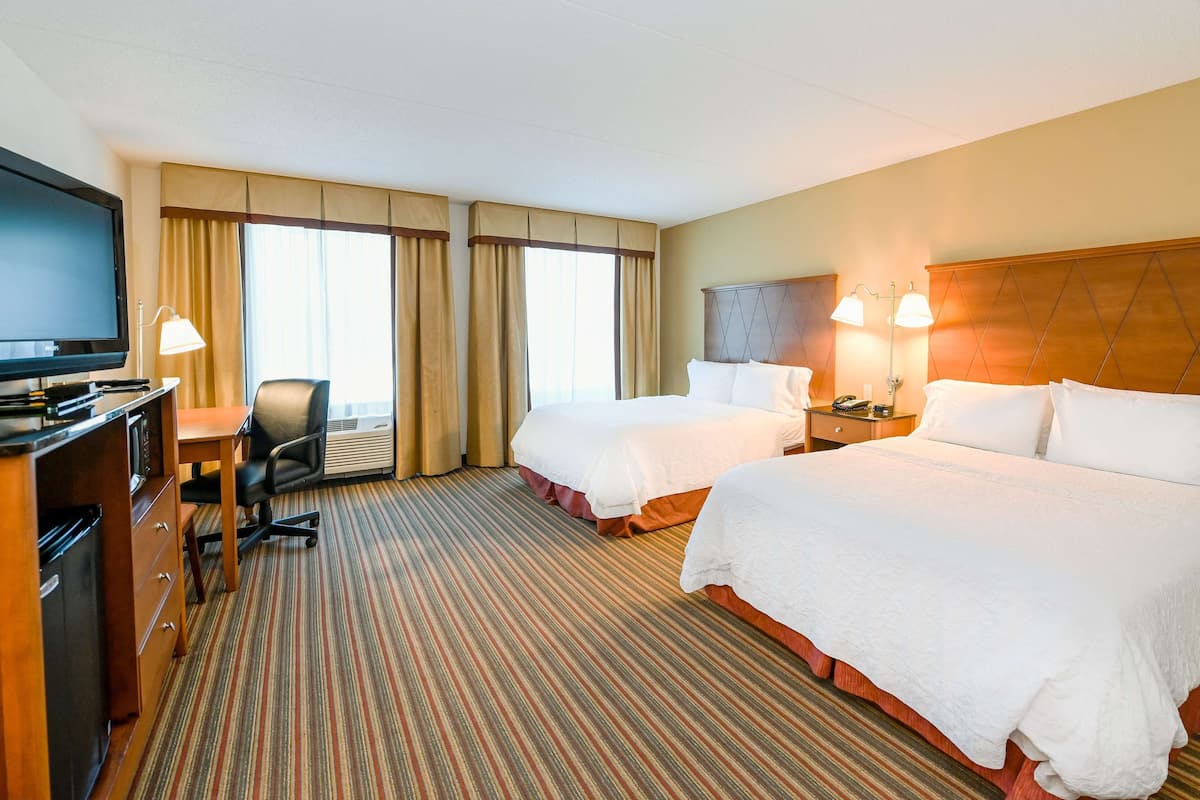 A hotel room with two beds, a desk with a television, and a chair.