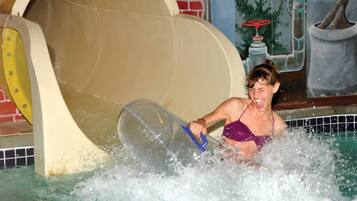 A person in a purple swimsuit in a water park with a large slide and a mural in the background.
