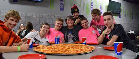 A group of people around a table with a large pizza and Pepsi cups.