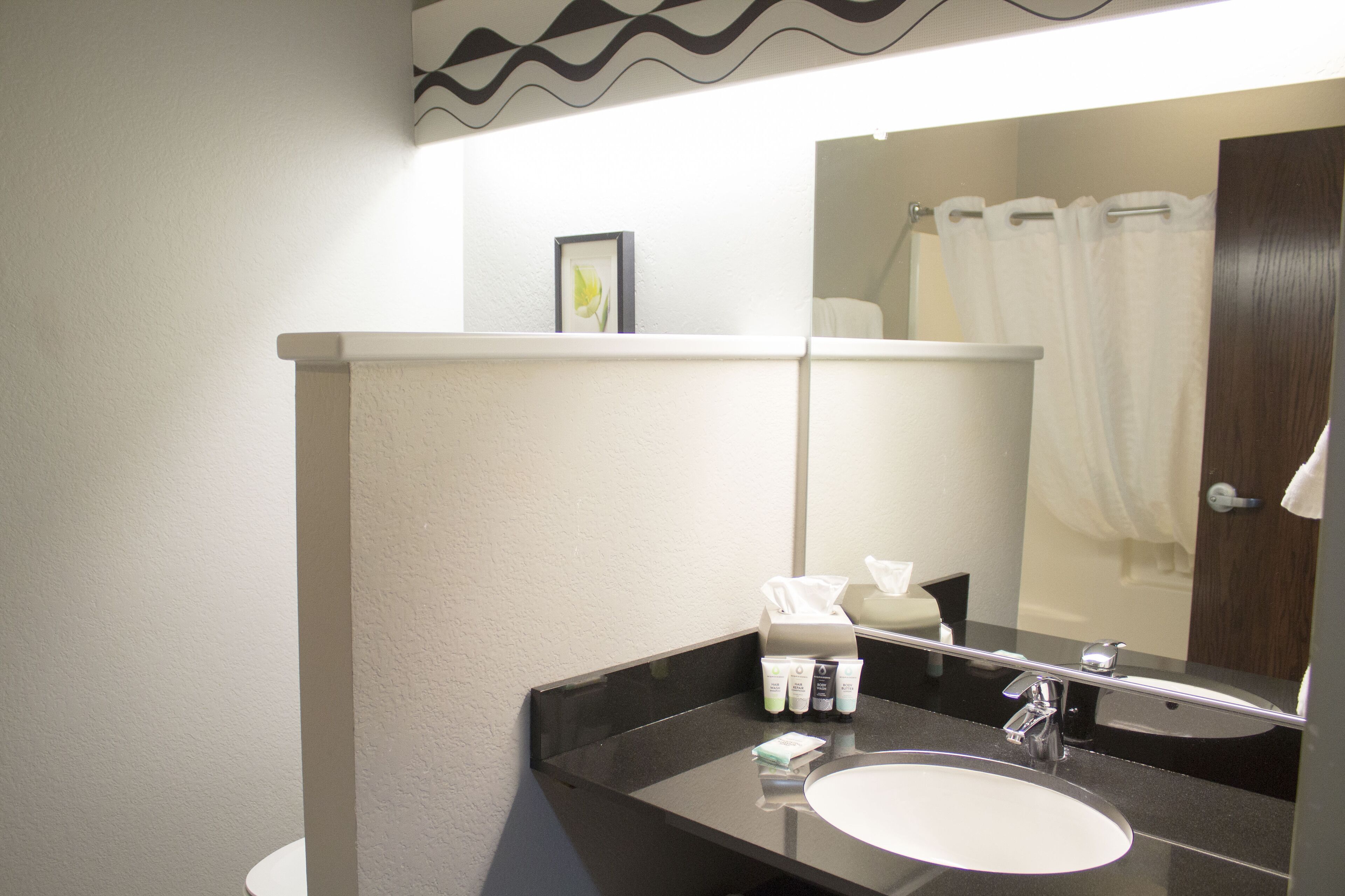 Un baño con lavamanos blanco, un espejo y repisas con artículos de aseo.