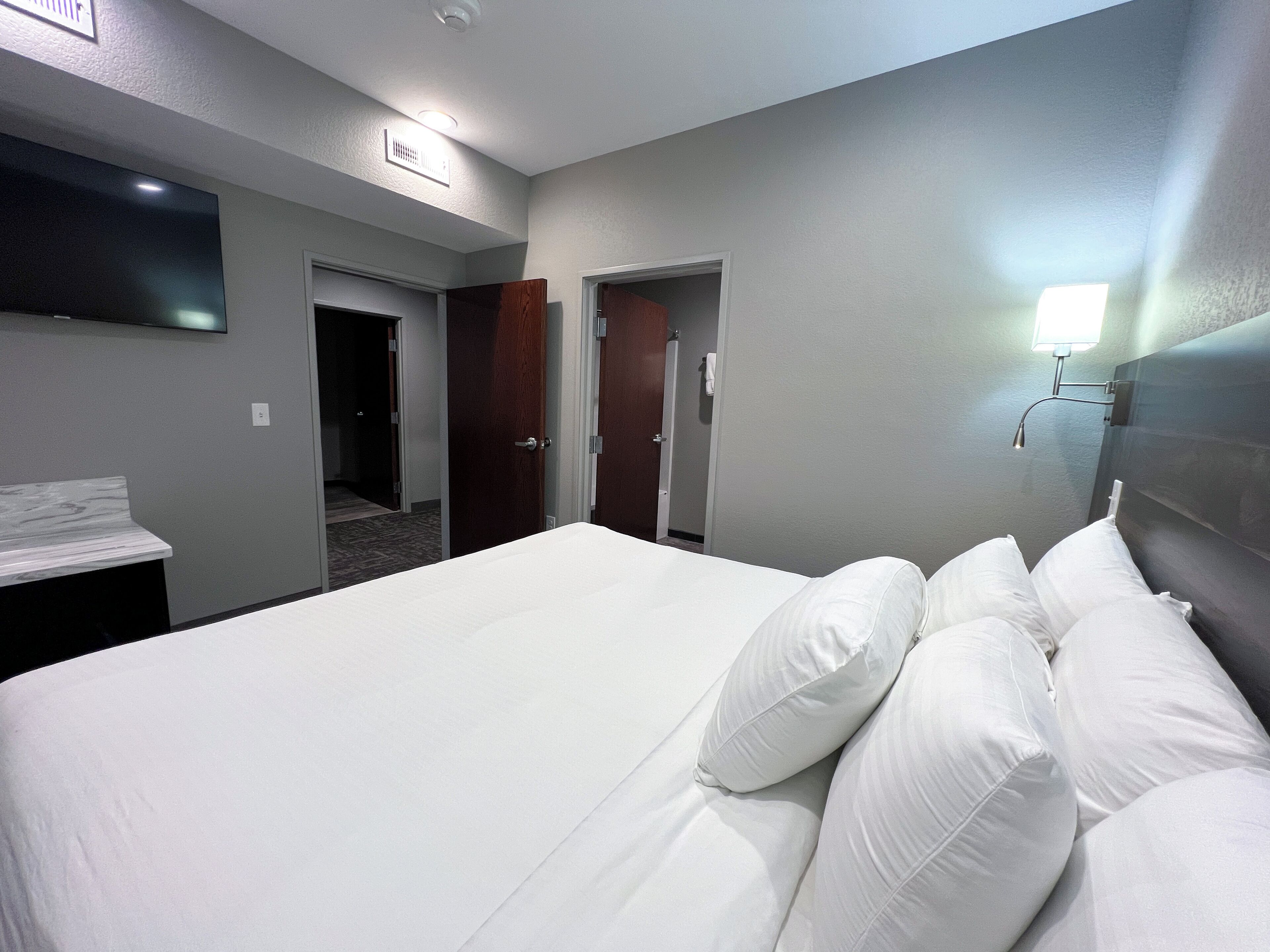 Ein Hotelzimmer mit einem großen Bett, einem an der Wand montierten Flachbildfernseher und einer Tür zu einem Badezimmer.