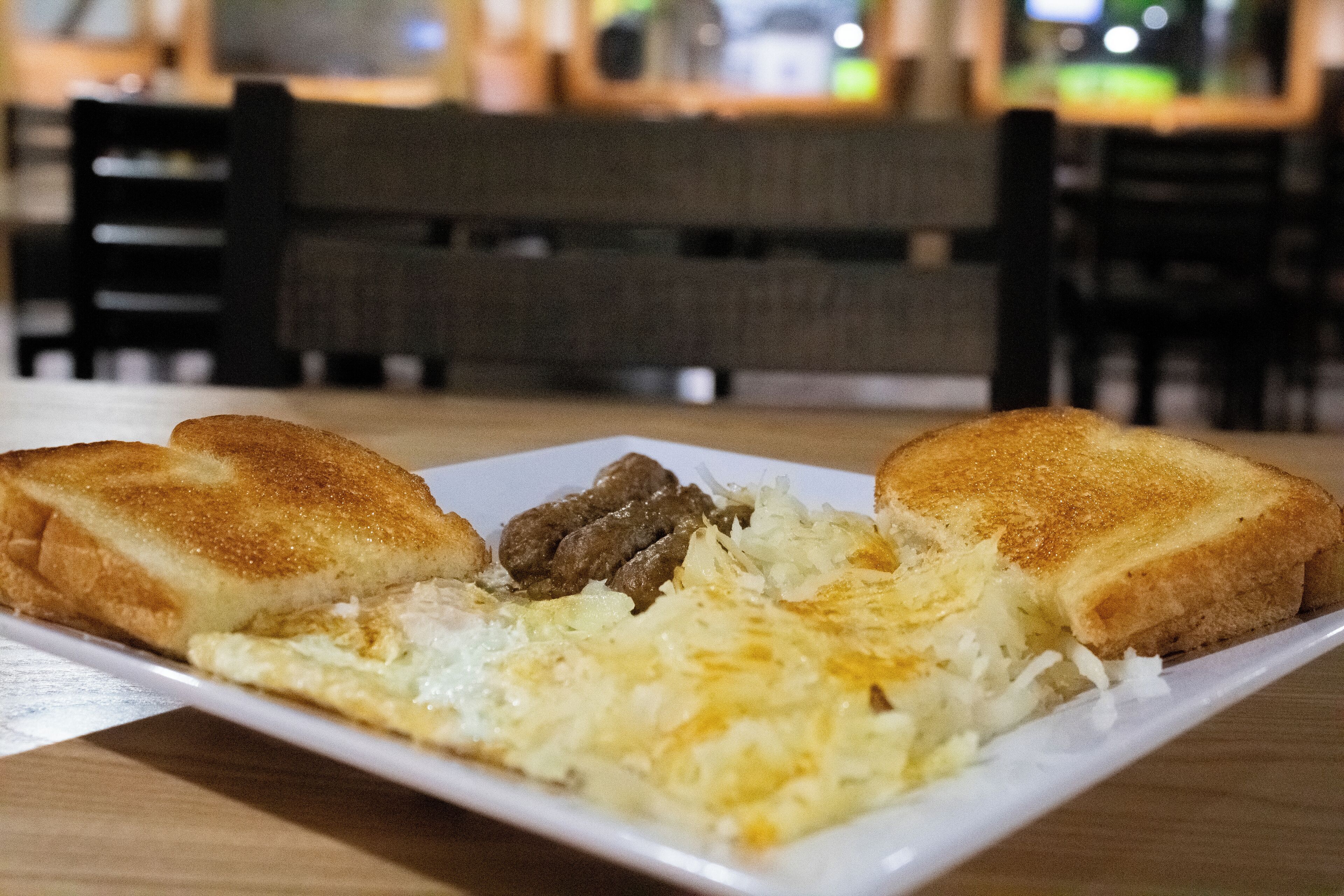 A plate of food with two slices of toast, a fried egg, and some meat on a white plate.