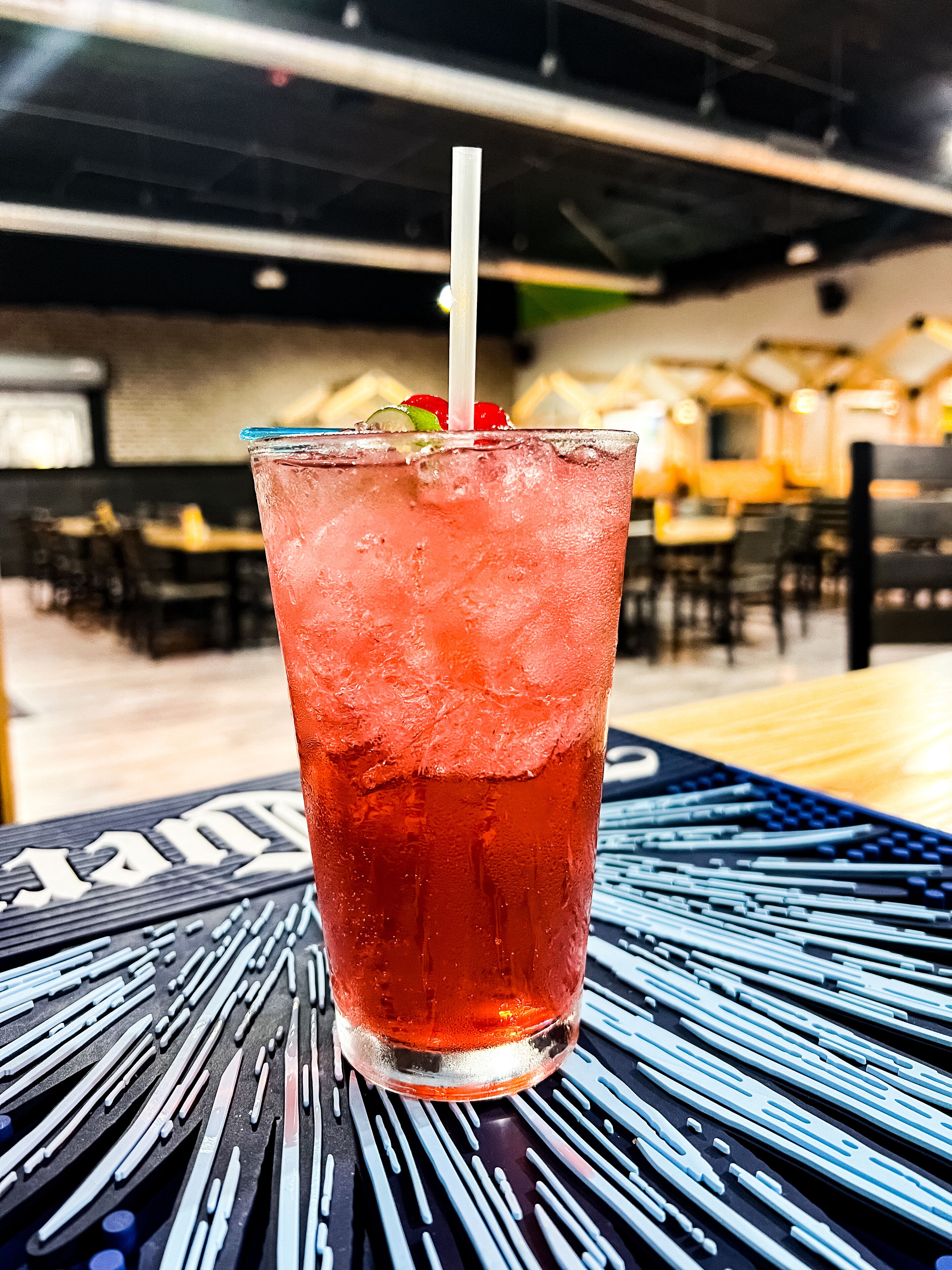 A glass of iced beverage with a straw, garnished with a cherry and mint, on a table with a black and blue pattern.