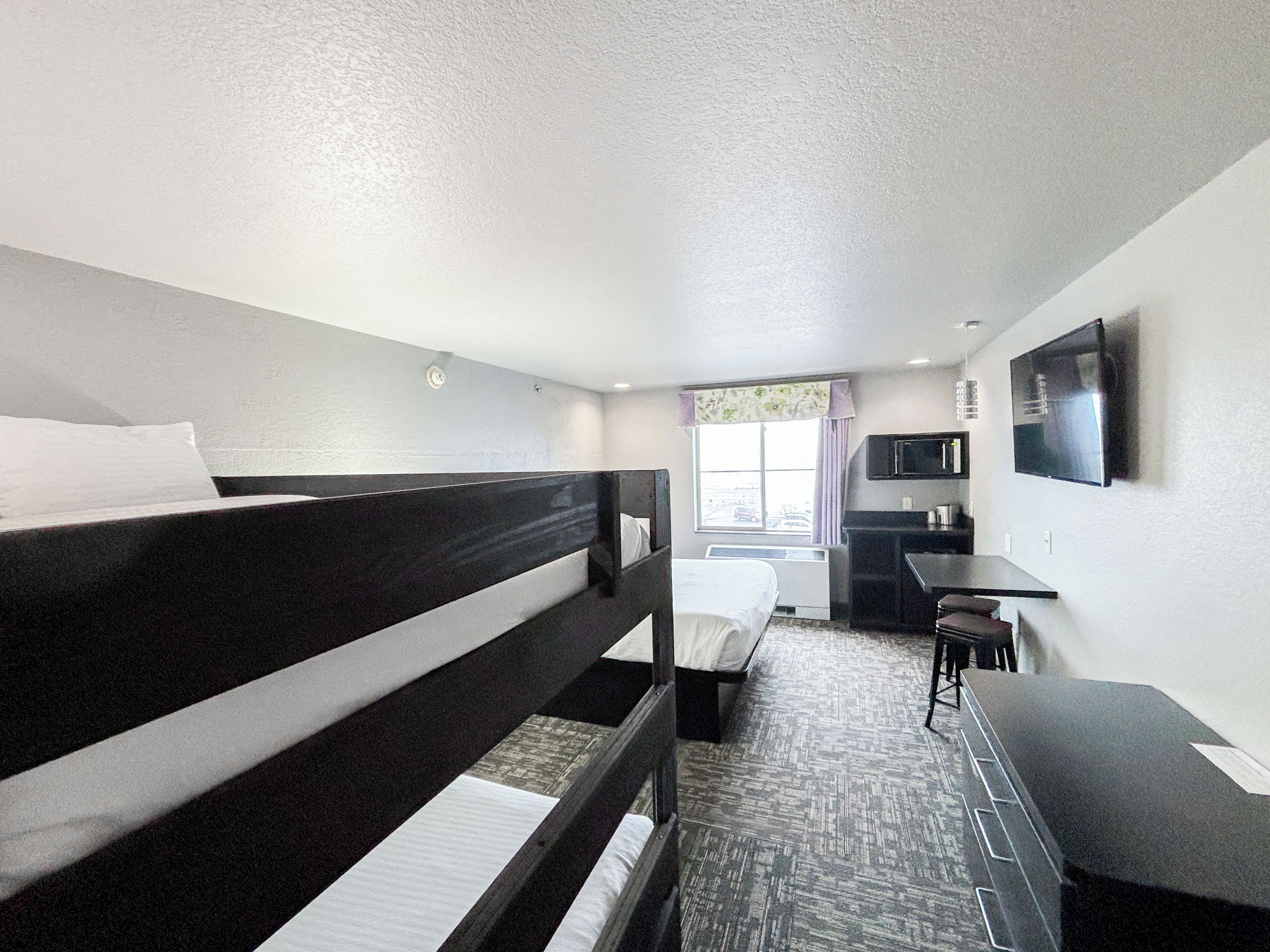 A hotel room with two single beds, a desk, a chair, a television, and a window with curtains.