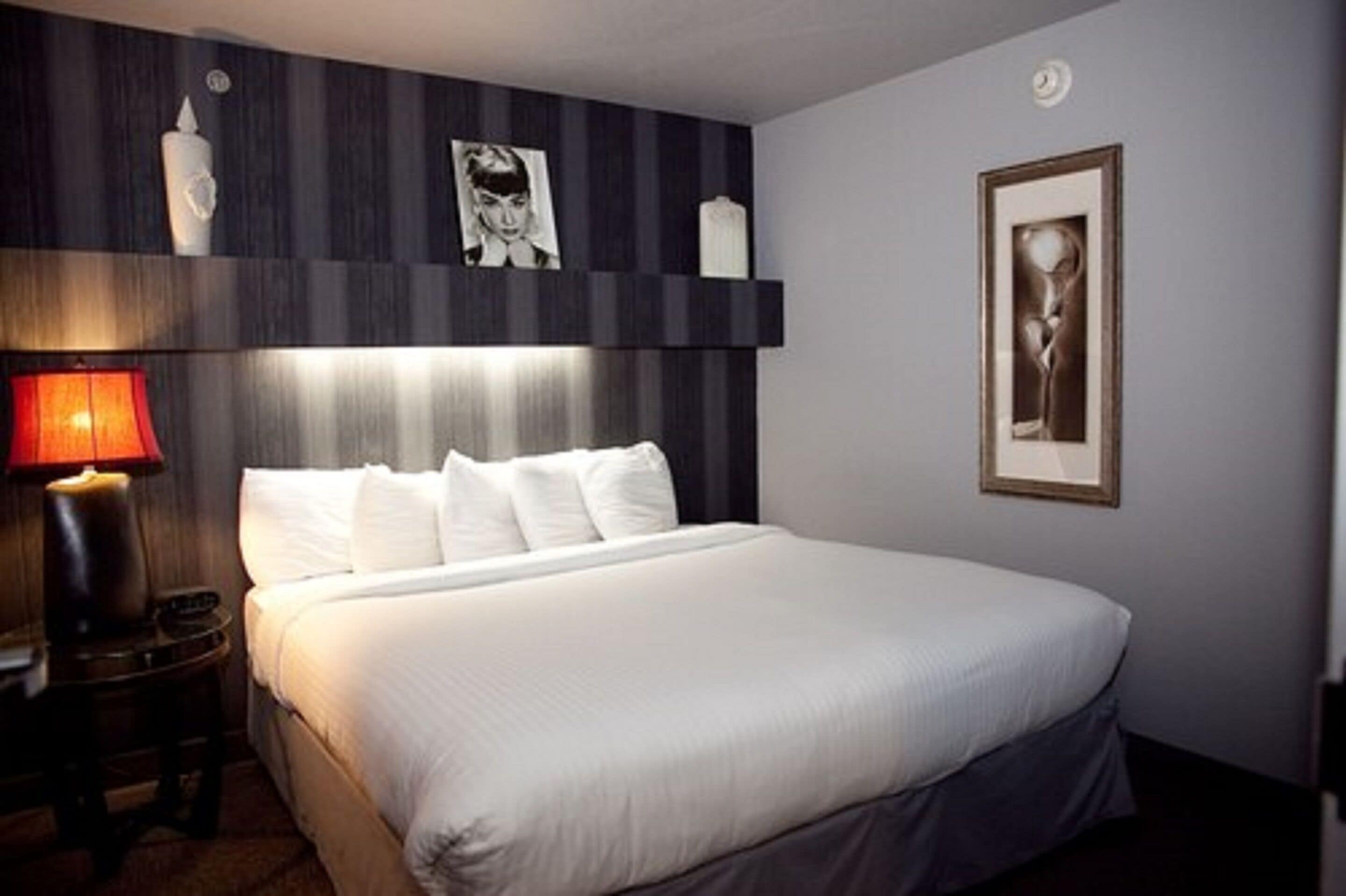 A hotel room with a large bed, a bedside table with a lamp, and artwork on the walls.