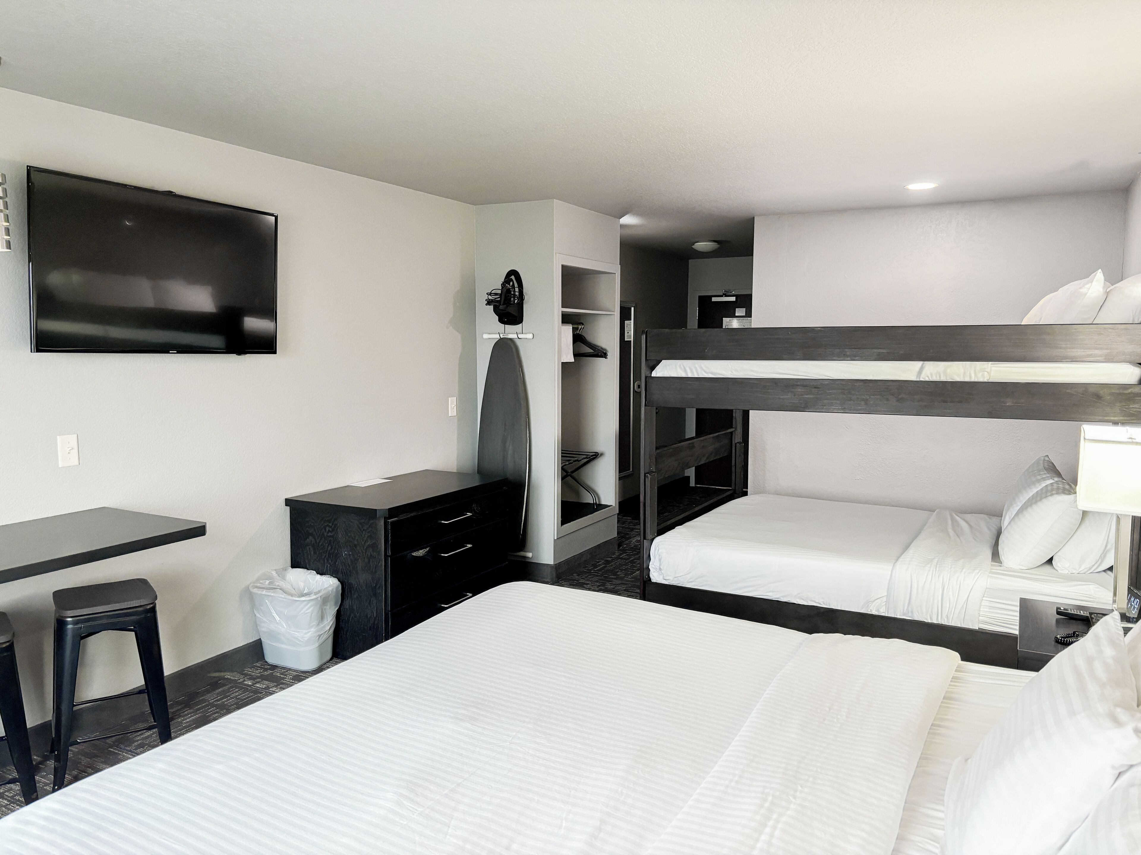Habitación de hotel con literas, un escritorio con silla, un televisor montado en la pared y un pequeño cubo de basura.