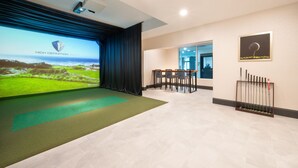 A modern conference room with a large screen displaying a golf course, a green carpet, a table with chairs, and a fire extinguisher mounted on the wall. - SPRINGHILL SUITES BY MARRIOTT CONYERS (Conyers)