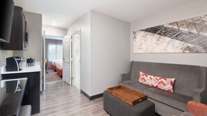 A modern hotel room with a grey sofa, a wooden coffee table, a desk with a computer, and a large abstract painting on the wall. - SPRINGHILL SUITES BY MARRIOTT CONYERS (Conyers)