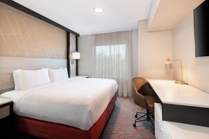 Habitación de hotel con una cama grande, un escritorio, una silla, un televisor y una ventana con cortinas.