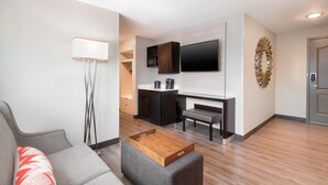 A modern living room with a grey sofa, a wooden coffee table, and a flat-screen TV mounted on the wall. - SPRINGHILL SUITES BY MARRIOTT CONYERS (Conyers)