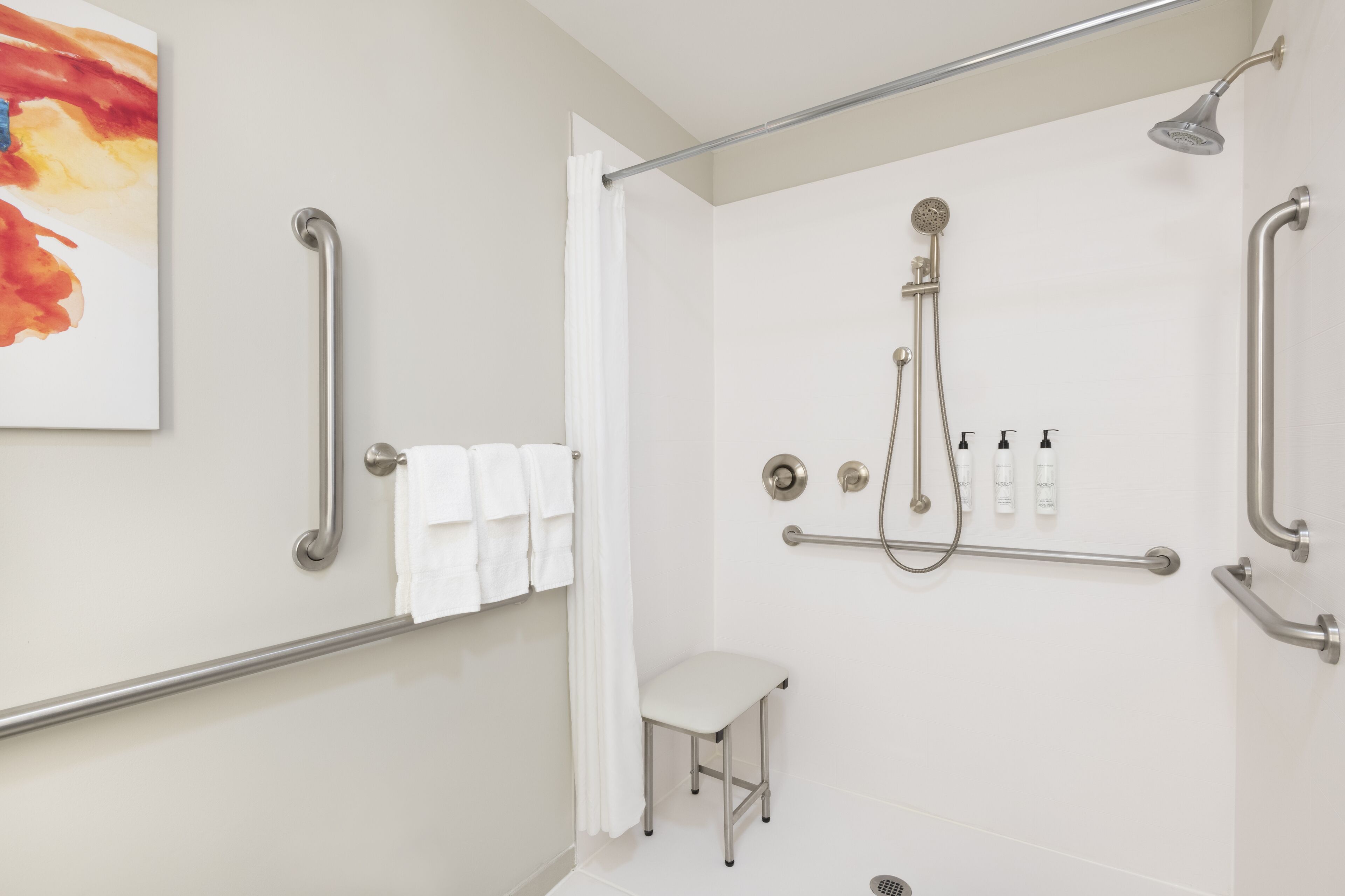 A modern bathroom with a shower, grab bars, a white toilet, and a small stool.