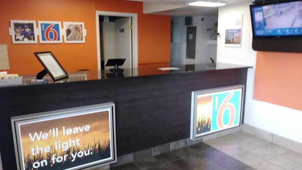 A reception area with a dark reception desk, a large screen displaying a motivational message, and a number '6' prominently displayed on the wall. - Motel 6 Goodland, KS (Goodland)