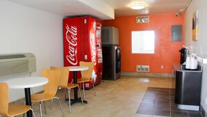 A compact kitchen with a refrigerator, a microwave, and a coffee machine. There are two tables with chairs, and a large Coca-Cola vending machine. - Motel 6 Goodland, KS (Goodland)