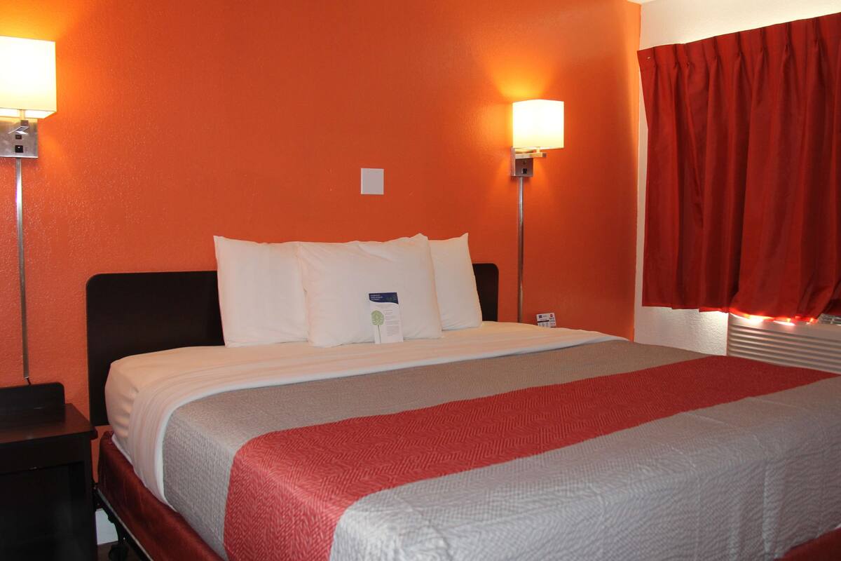 A hotel room with a large bed, two bedside lamps, and a red curtain.