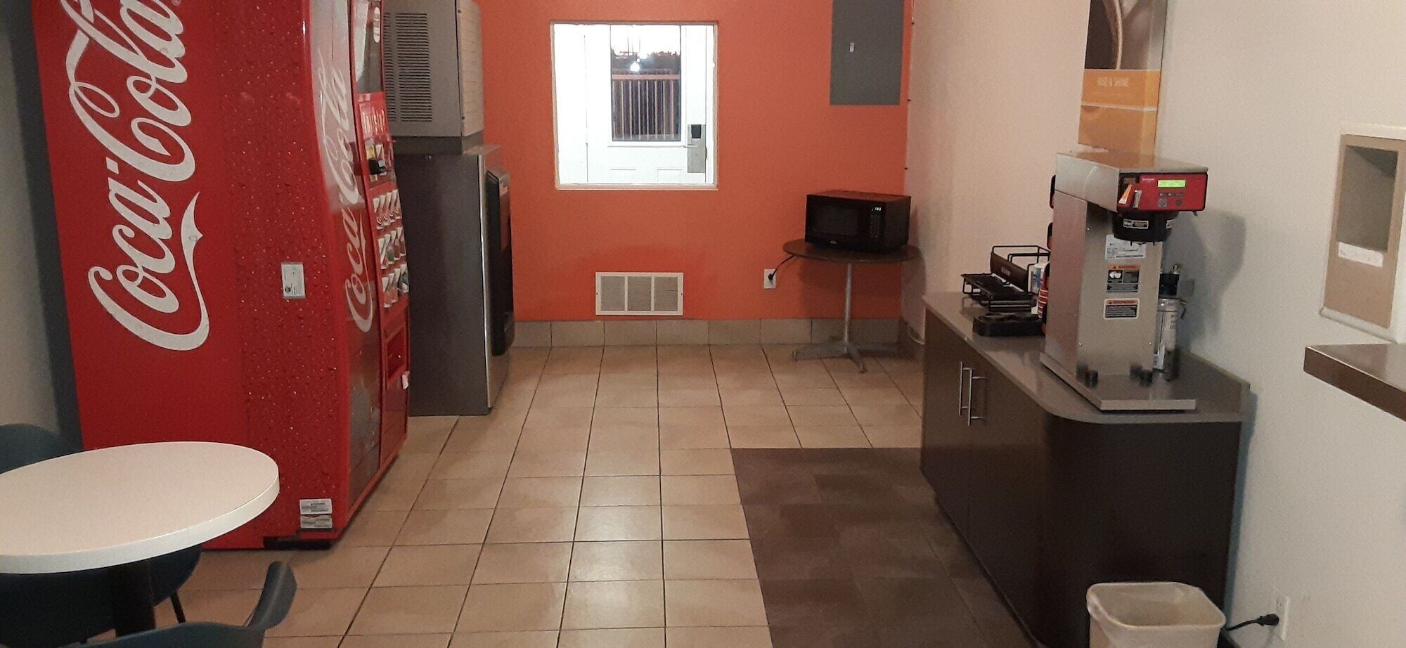 A kitchen with a Coca-Cola refrigerator, a microwave, a coffee machine, and a window with a view.