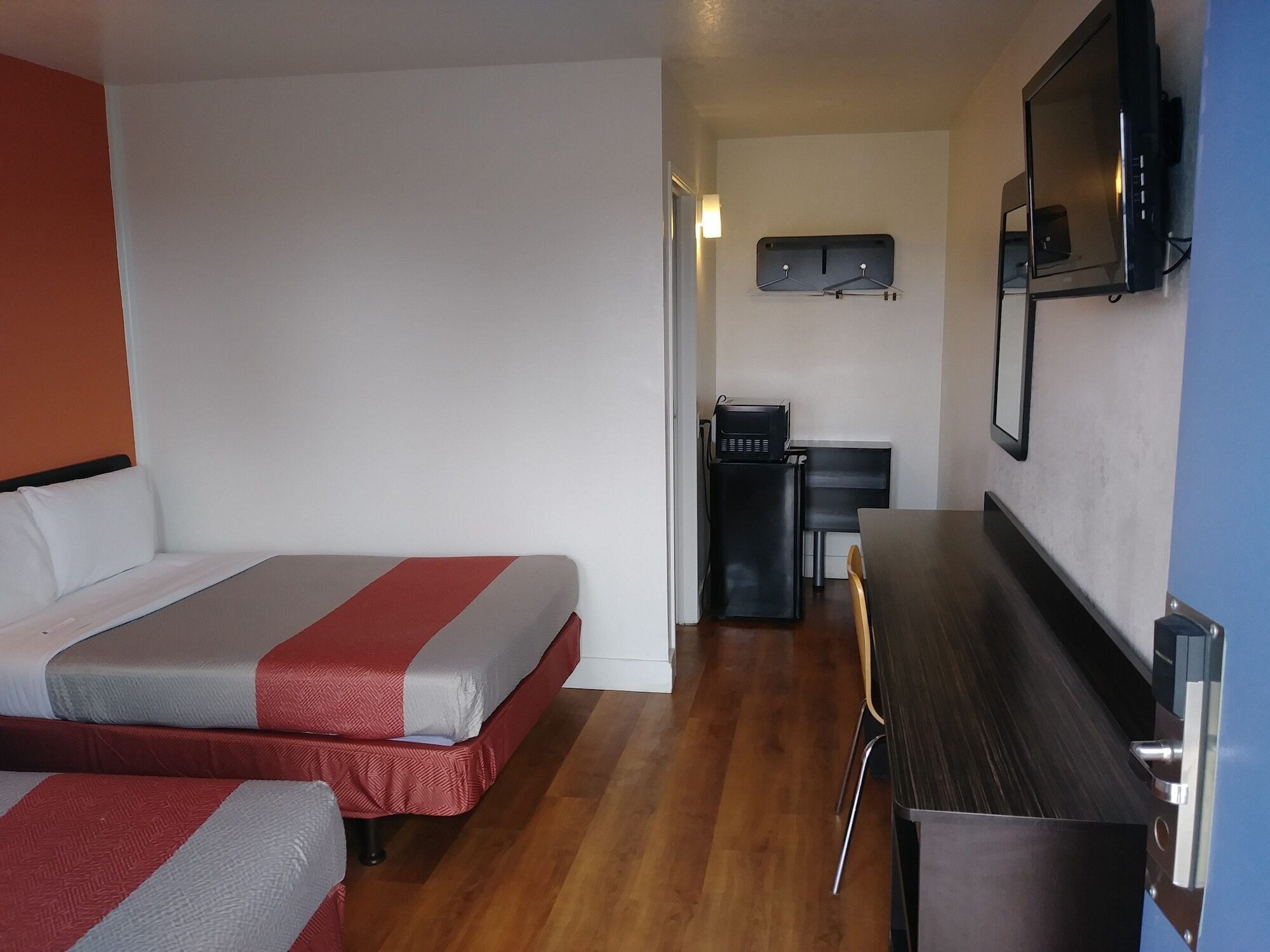 A hotel room with two beds, a desk, a chair, a microwave, and a TV.