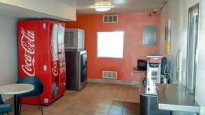A compact kitchen with a red Coca-Cola vending machine, a refrigerator, a window, and a small table with chairs. - Motel 6 Goodland, KS (Goodland)