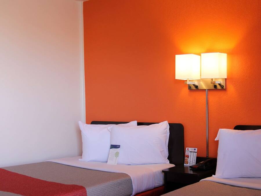 A hotel room with two beds, a nightstand with a lamp, and a wall-mounted phone.