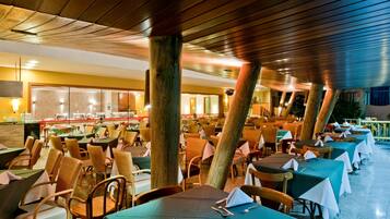 A spacious restaurant with multiple tables and chairs, wooden pillars, and a buffet area.
