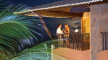 Una pareja en un balcón con vista al cielo nocturno y hojas de palmera al frente.