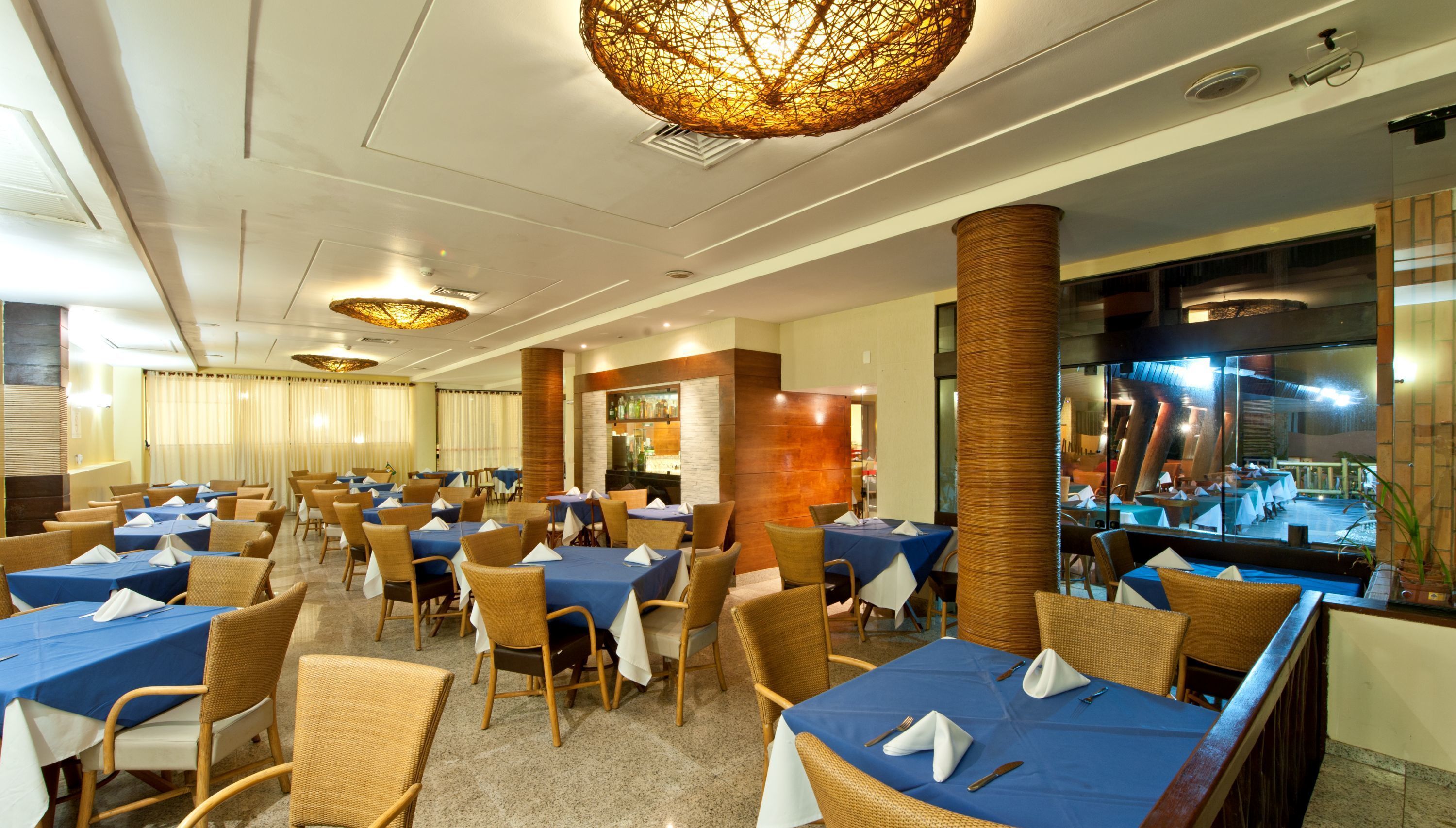Comedor de hotel con varias mesas y sillas, zona de bar y vista a la piscina exterior.