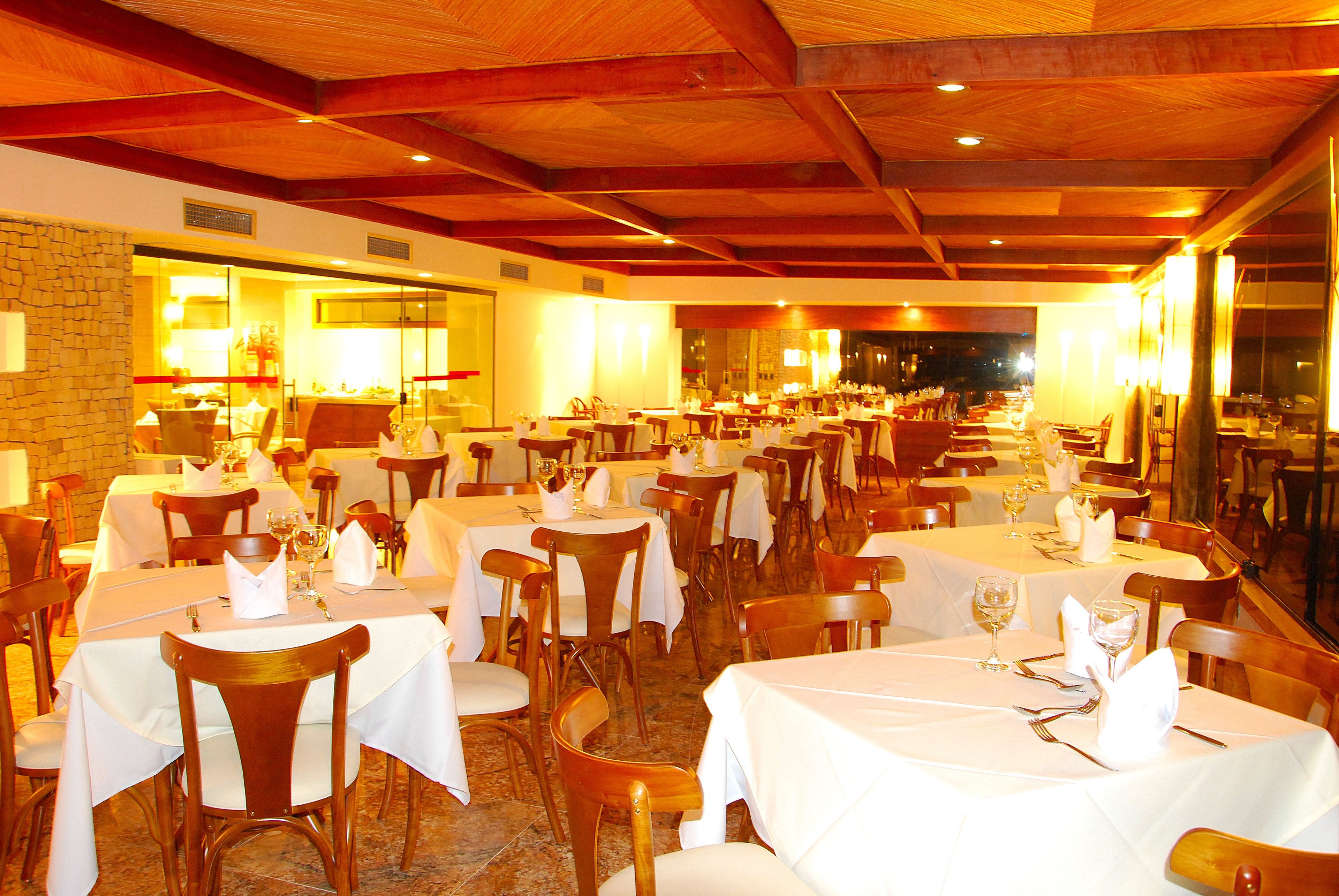 A restaurant with multiple tables and chairs, wooden beams on the ceiling, and a stone wall.