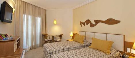 Habitación de hotel con dos camas, un escritorio, una silla, un televisor y una obra de arte en la pared.