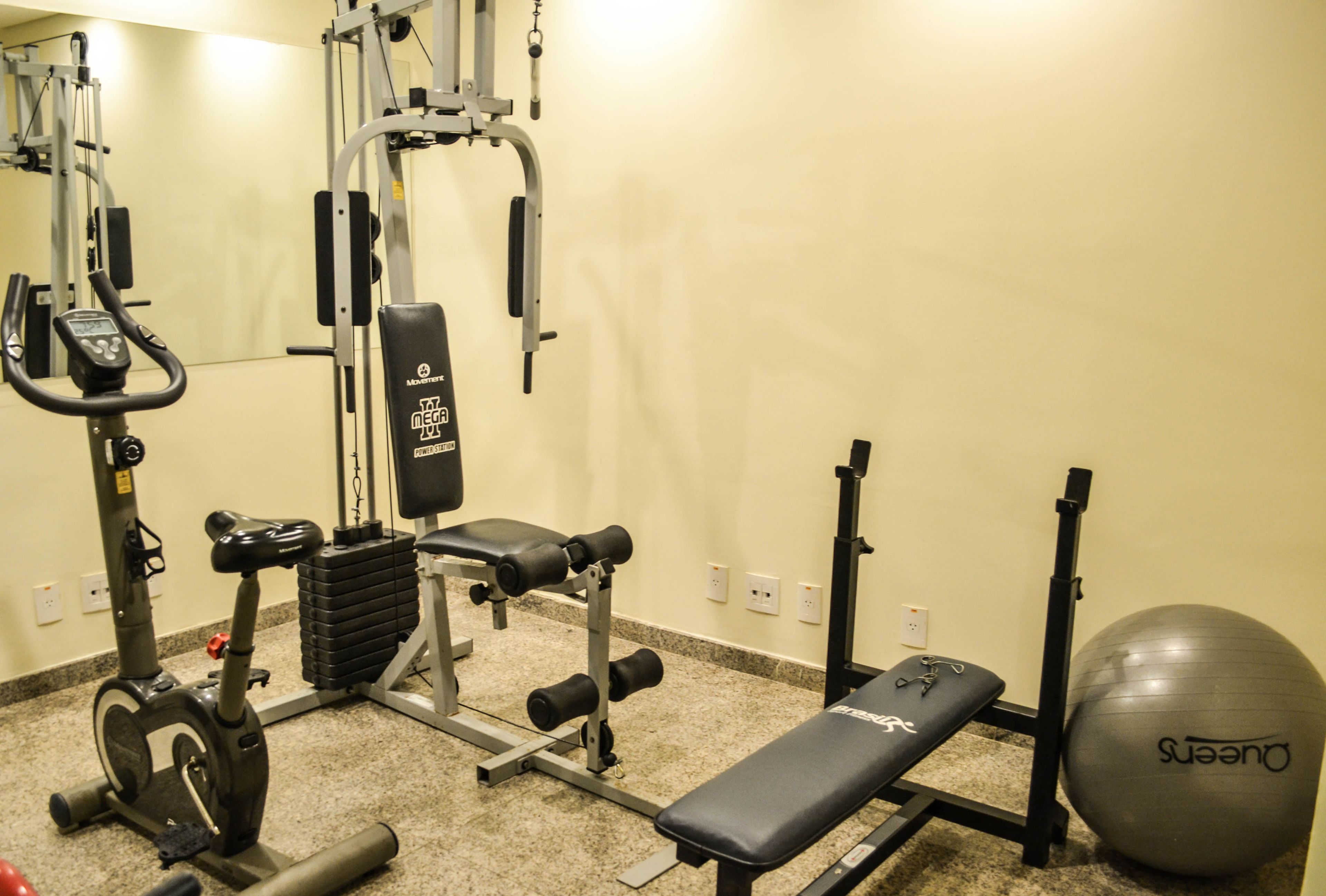 A gym with exercise equipment including a stationary bike, a bench, a squat rack, and an exercise ball.