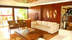 A modern living room with a white sofa, two armchairs, a wooden coffee table, and a large window offering a view of the outdoors.
