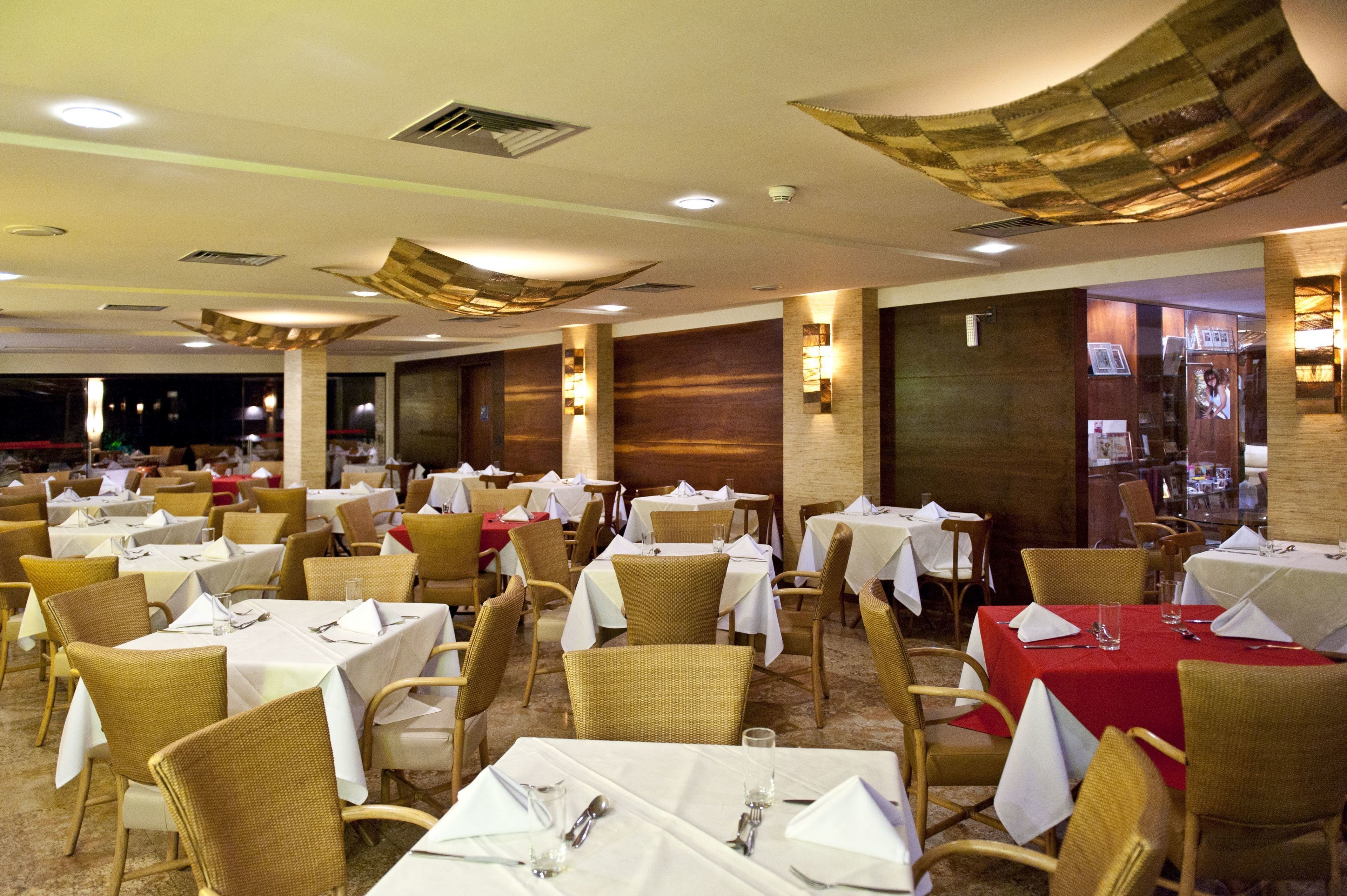 A restaurant with multiple tables and chairs, some with red tablecloths, and others with white.