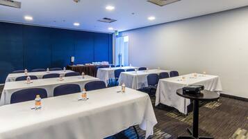 A conference room with multiple tables, chairs, and water bottles. There is an exit sign on the wall and a projector on one of the tables.