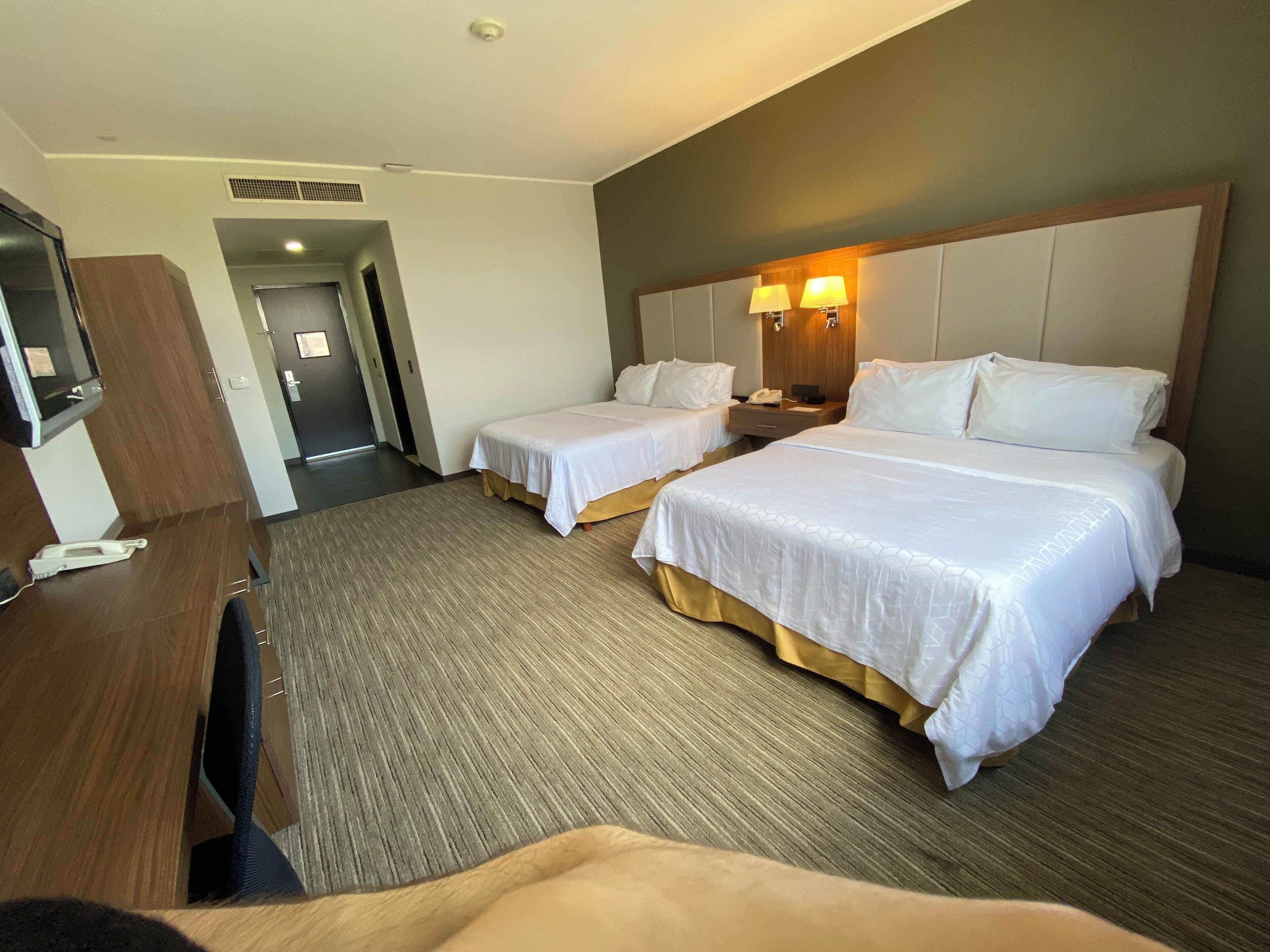 Habitación de hotel con dos camas, un escritorio, un televisor y la puerta del baño.