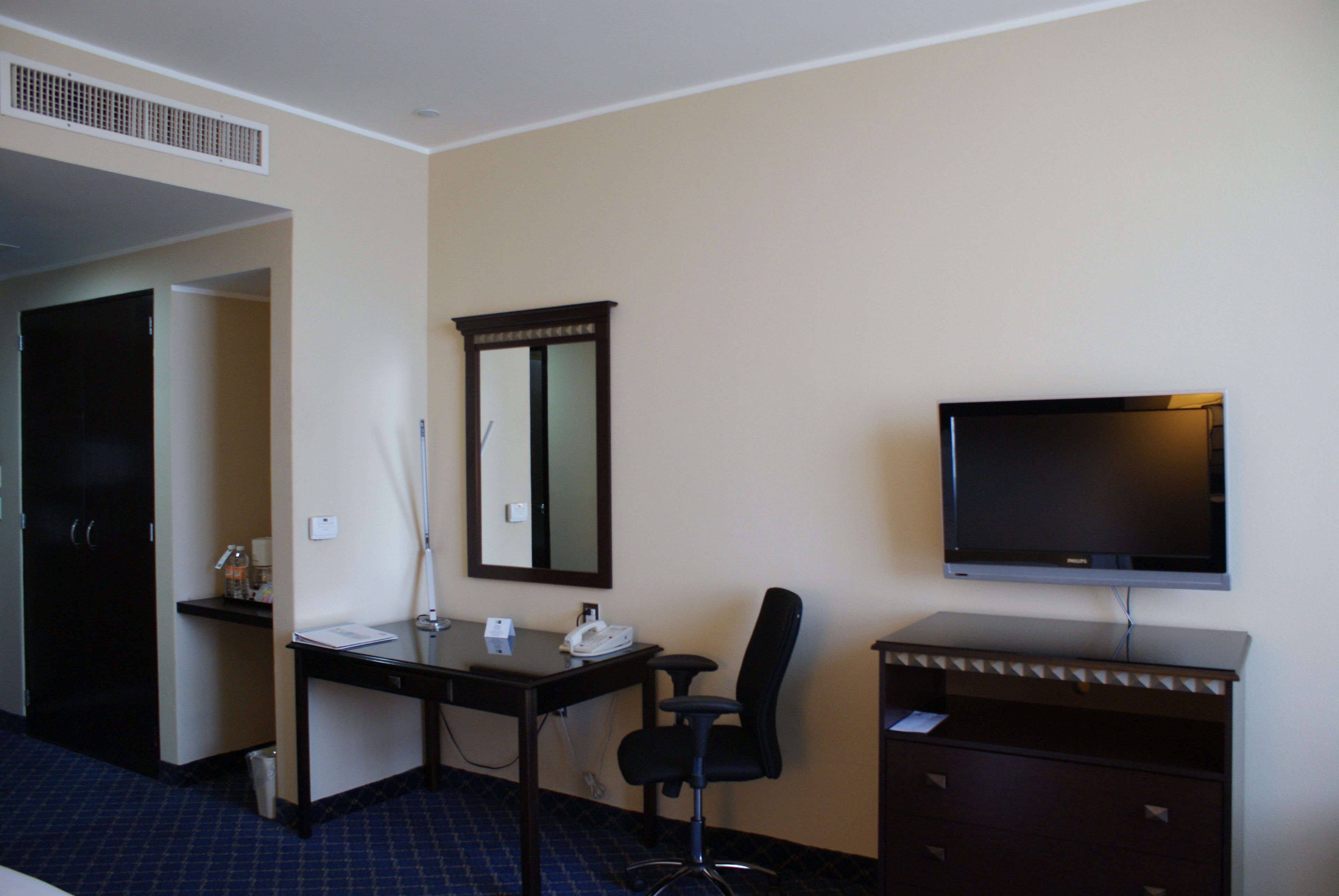 A hotel room with a desk, chair, television, and a wardrobe.
