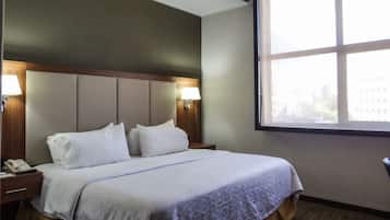 Une chambre d’hôtel avec un lit, deux lampes de chevet, une table de chevet avec un téléphone et une fenêtre donnant sur des immeubles.