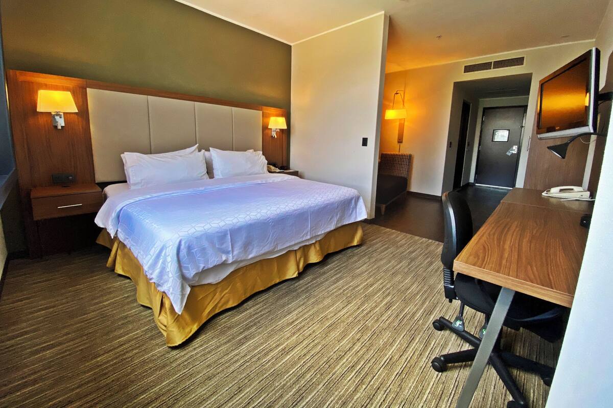 A hotel room with a bed, bedside tables, a desk, and a chair.